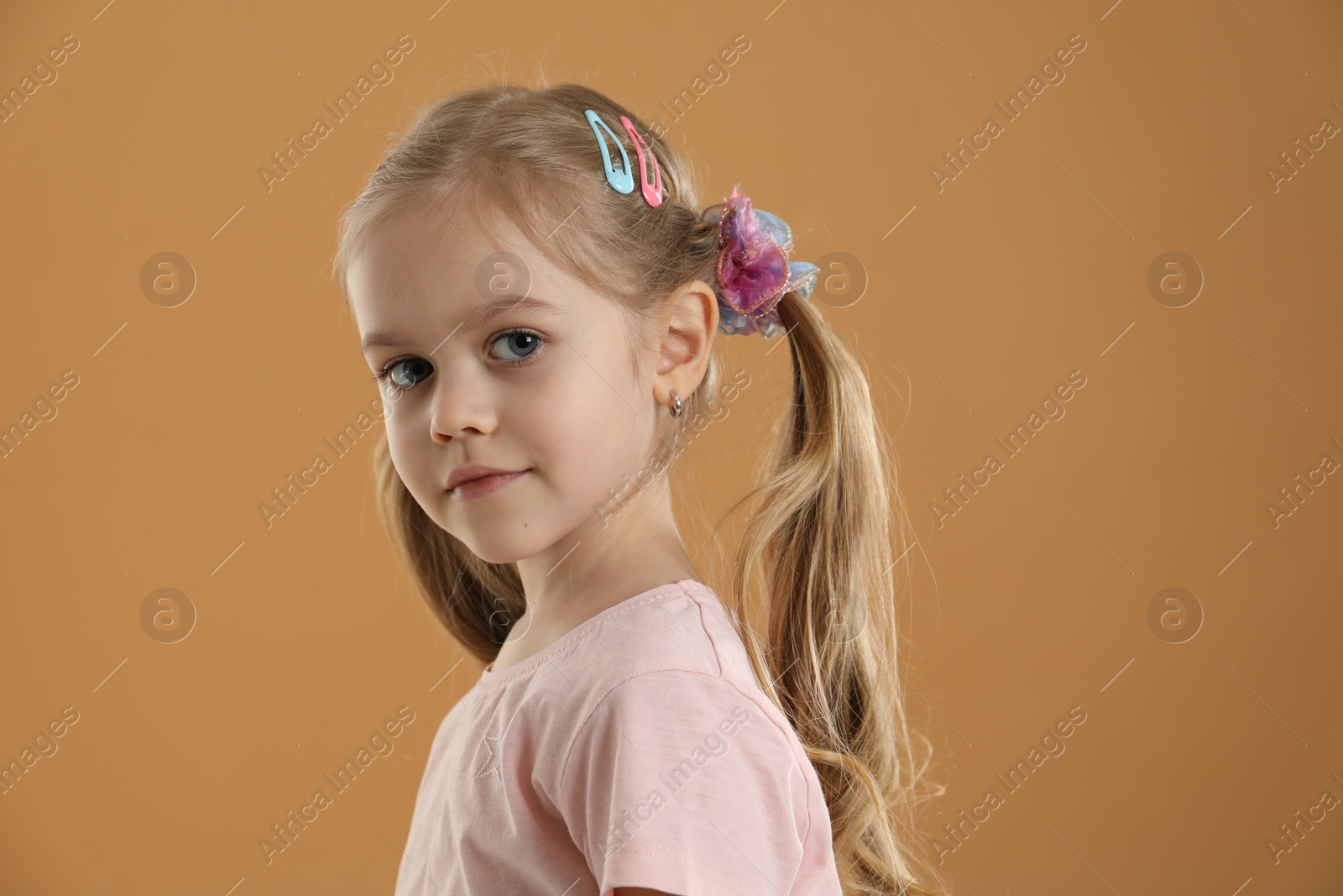 Photo of Cute little girl wearing beautiful hair accessories on light brown background