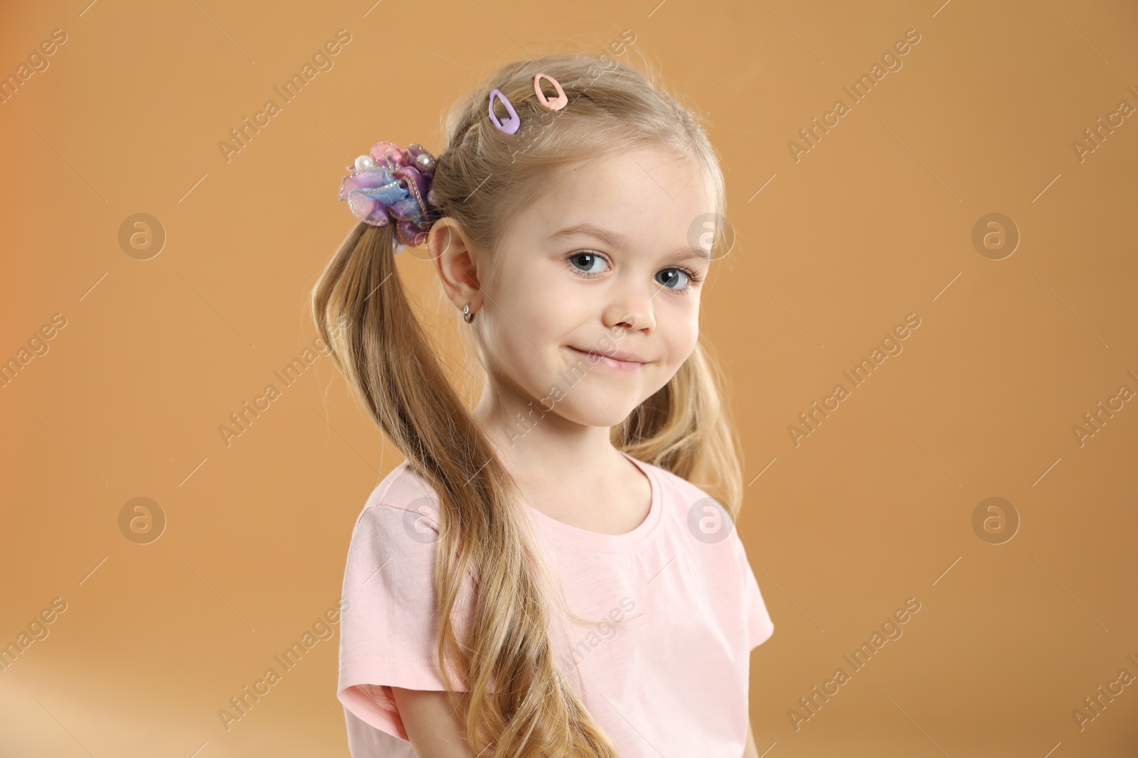 Photo of Cute little girl wearing beautiful hair accessories on light brown background