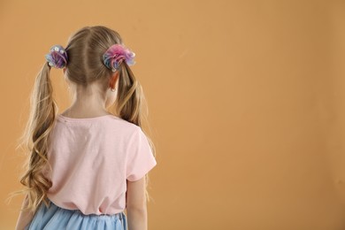 Photo of Cute little girl wearing beautiful hair accessories on light brown background, back view. Space for text