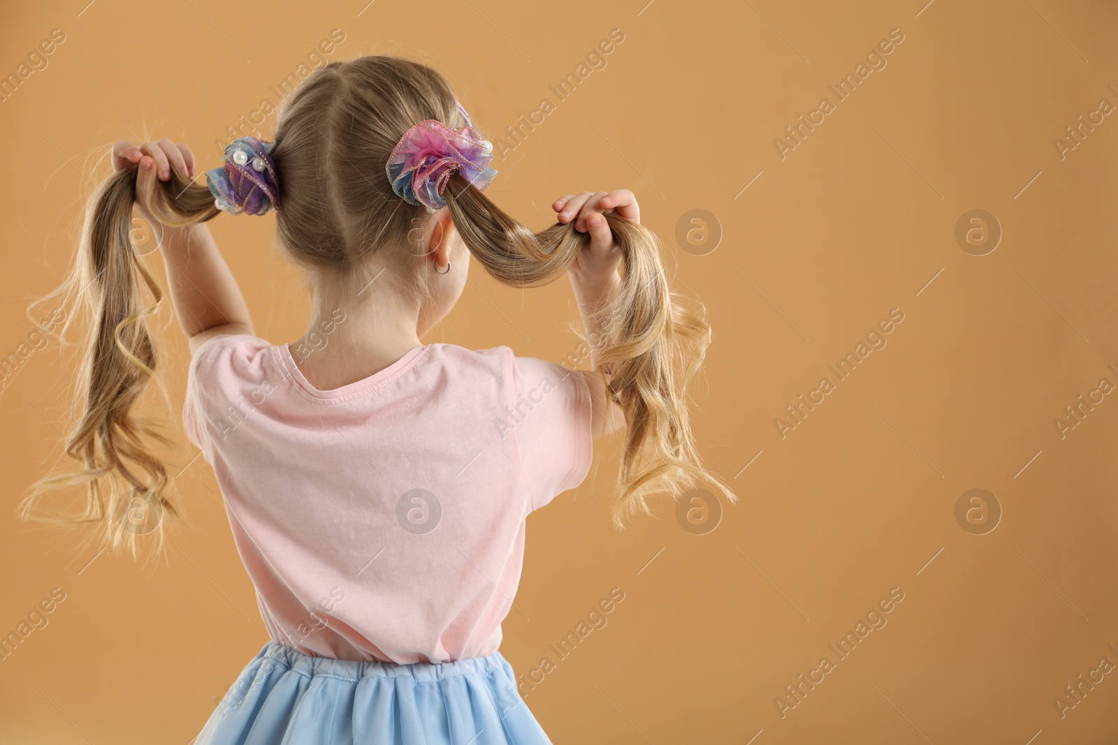 Photo of Cute little girl wearing beautiful hair accessories on light brown background, back view