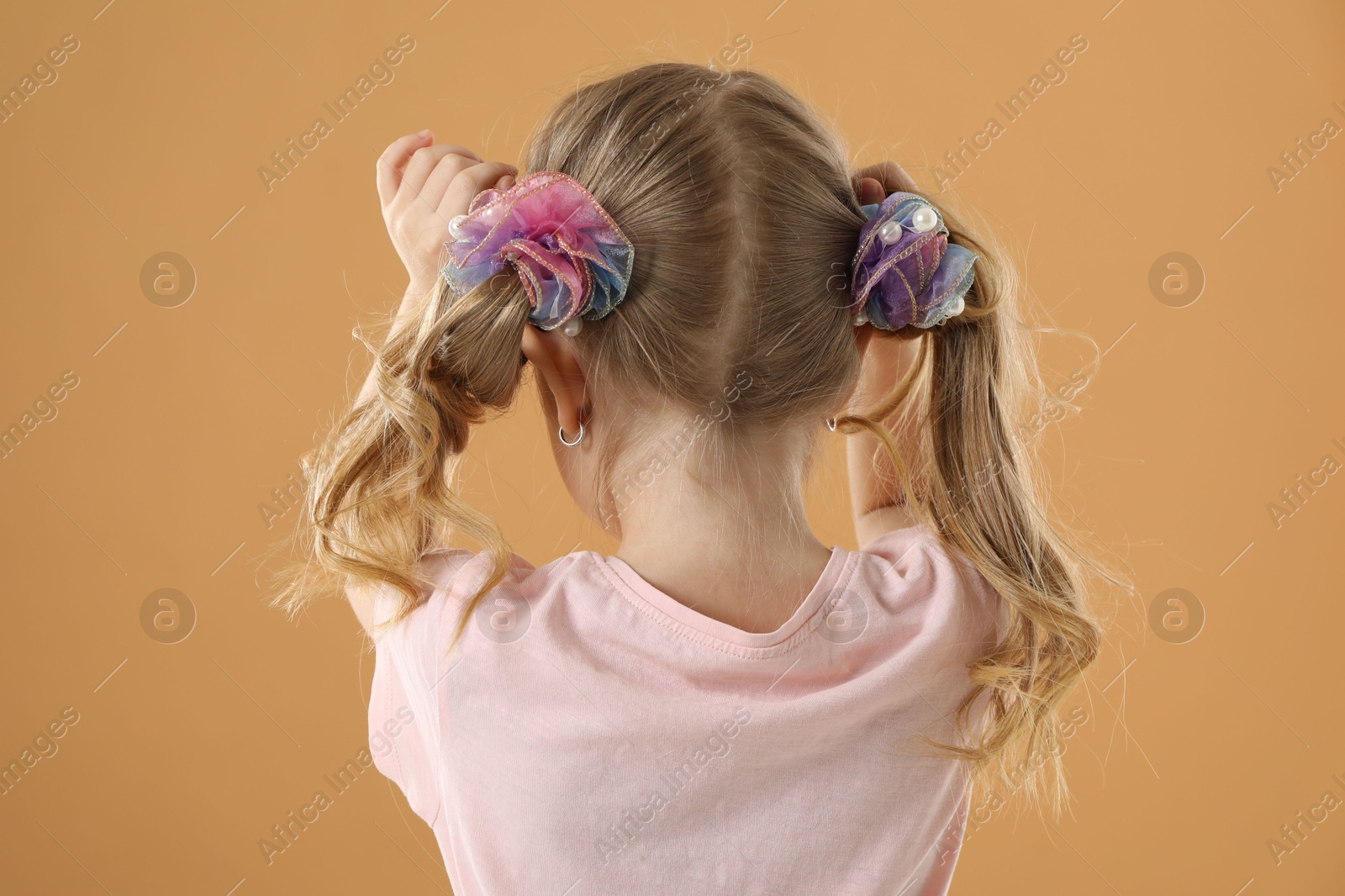 Photo of Cute little girl wearing beautiful hair accessories on light brown background, back view