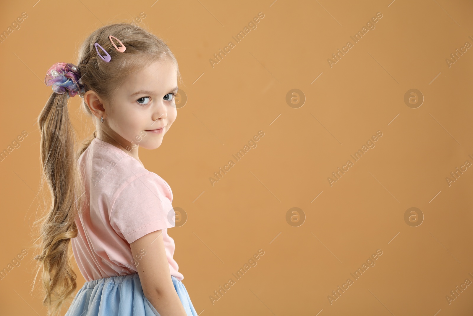 Photo of Cute little girl wearing beautiful hair accessories on light brown background. Space for text