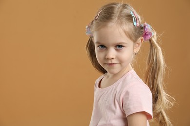 Photo of Cute little girl wearing beautiful hair accessories on light brown background. Space for text