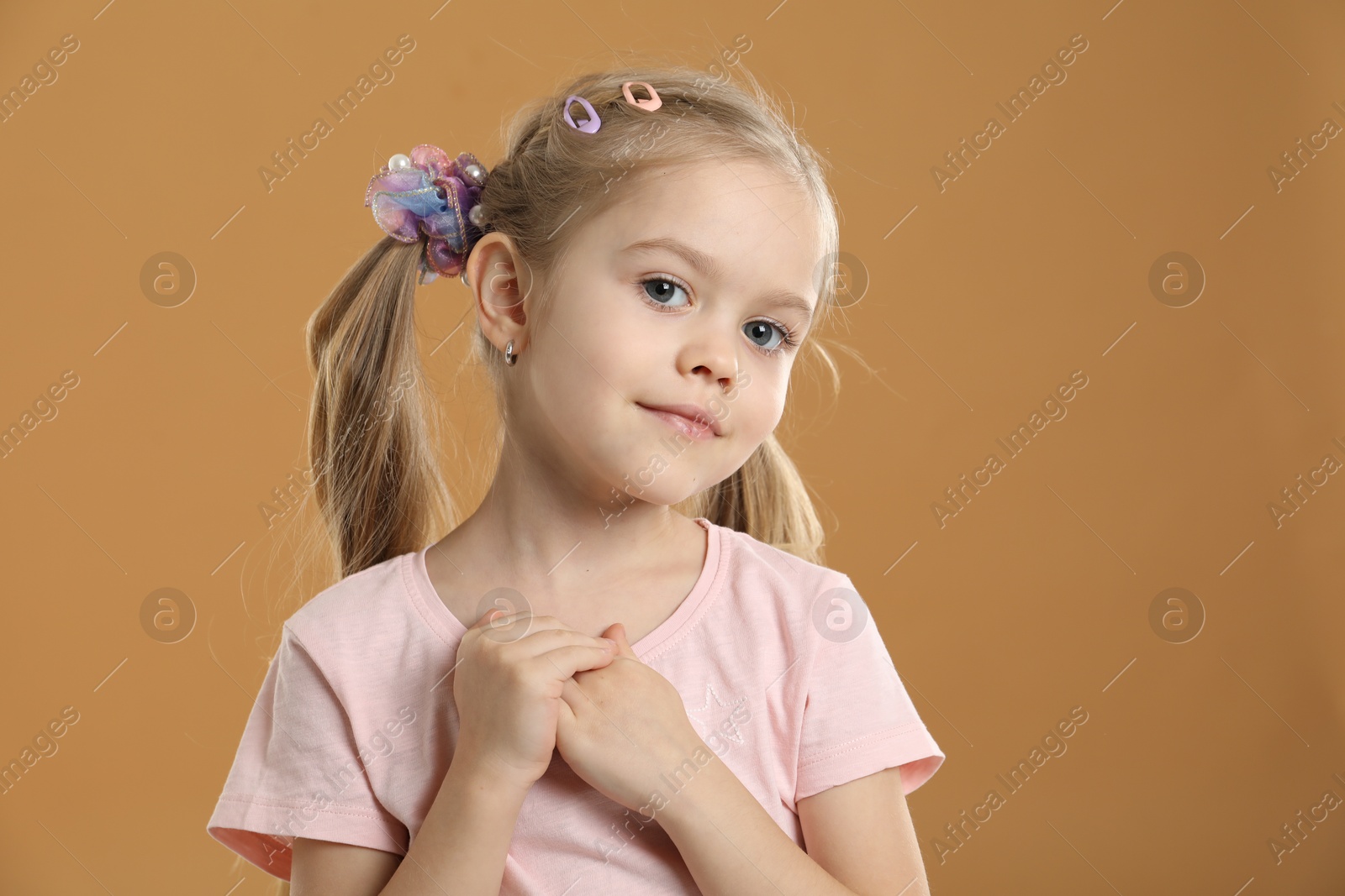 Photo of Cute little girl wearing beautiful hair accessories on light brown background