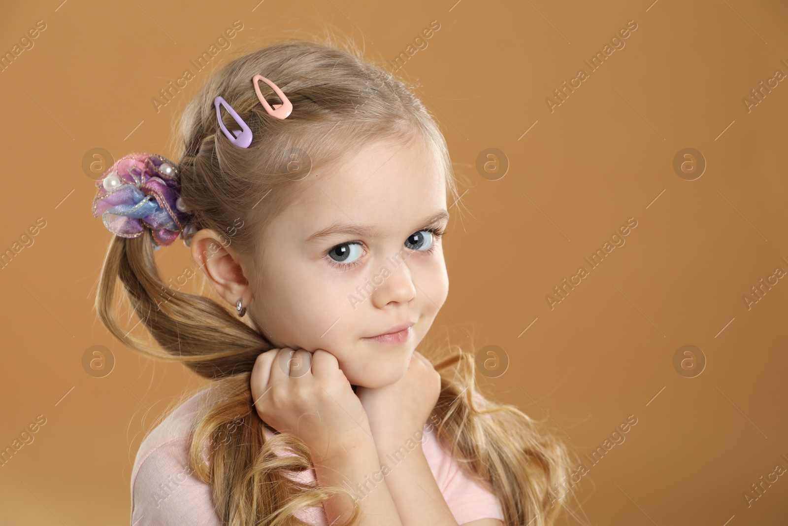 Photo of Cute little girl wearing beautiful hair accessories on light brown background. Space for text