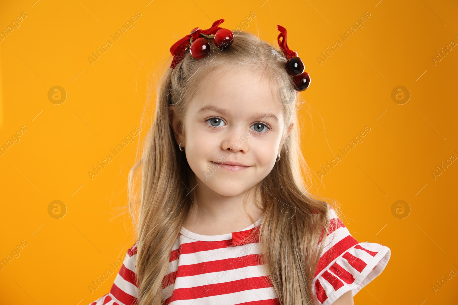 Photo of Cute little girl wearing beautiful bows with cherries on orange background