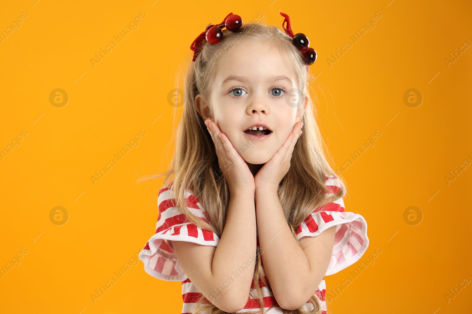 Photo of Cute little girl wearing beautiful bows with cherries on orange background