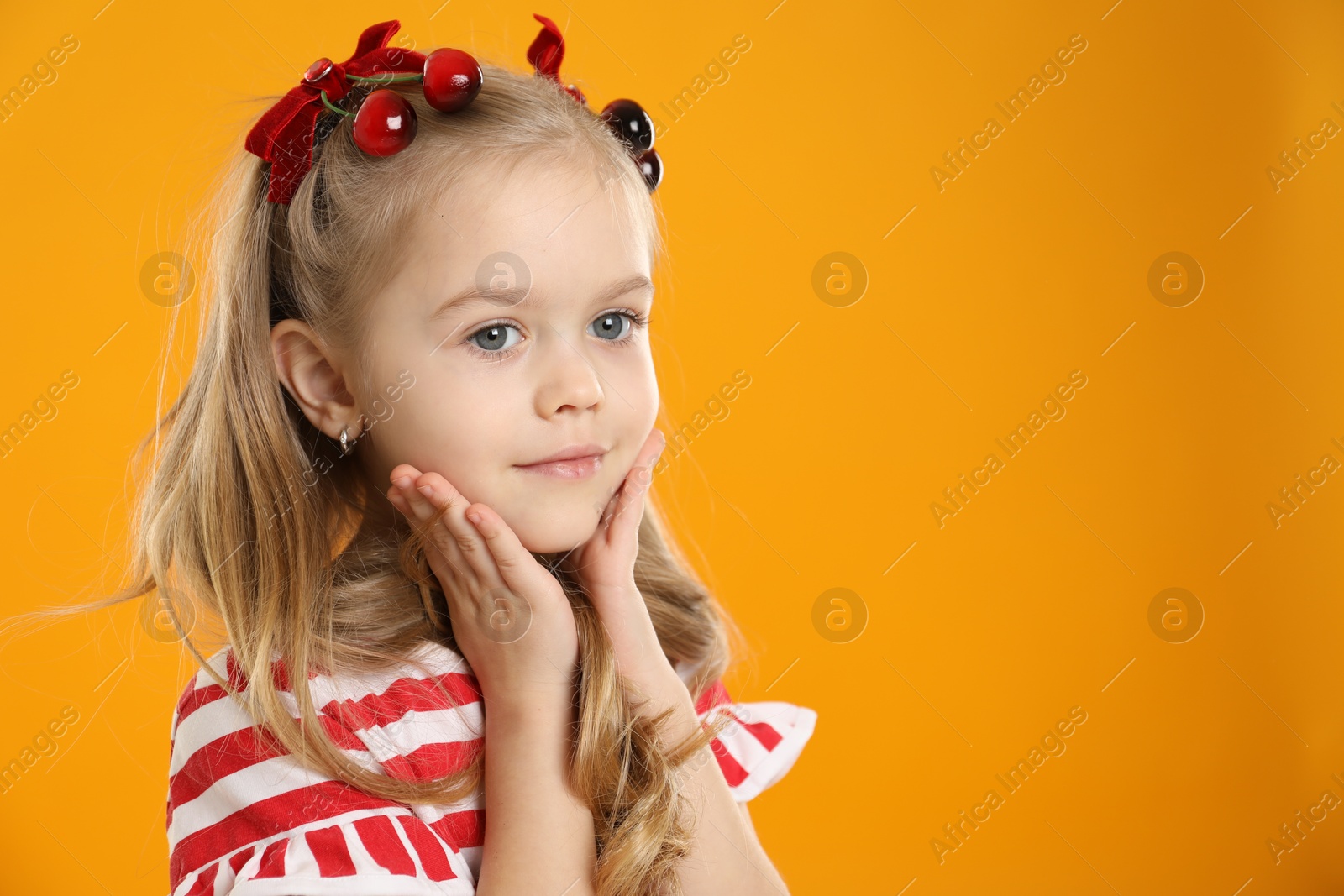 Photo of Cute little girl wearing beautiful bows with cherries on orange background. Space for text