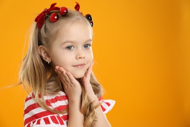 Photo of Cute little girl wearing beautiful bows with cherries on orange background. Space for text