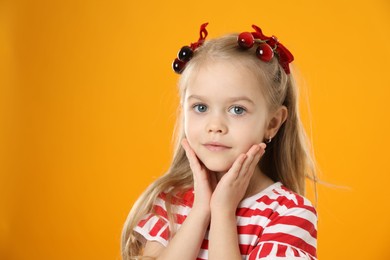 Photo of Cute little girl wearing beautiful bows with cherries on orange background. Space for text