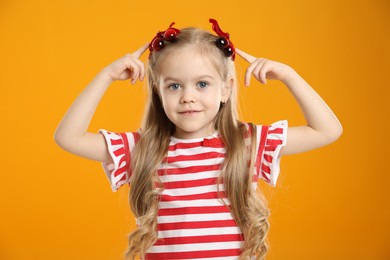 Photo of Cute little girl wearing beautiful bows with cherries on orange background