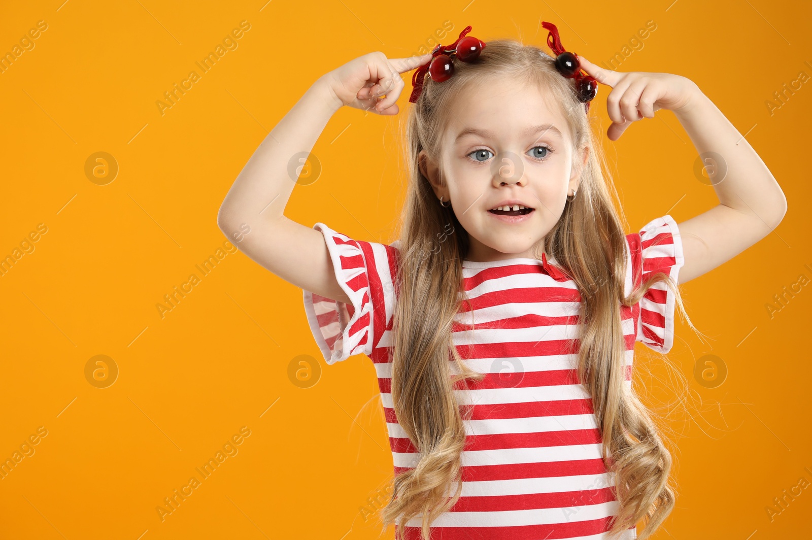 Photo of Cute little girl wearing beautiful bows with cherries on orange background