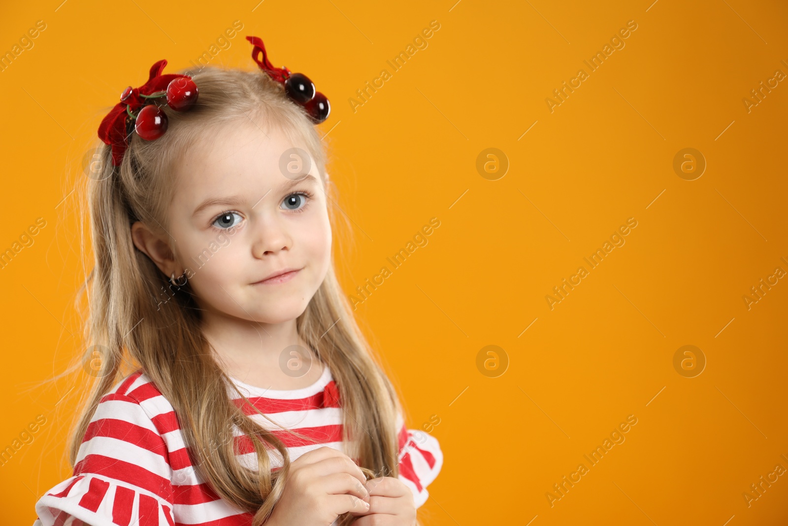 Photo of Cute little girl wearing beautiful bows with cherries on orange background. Space for text