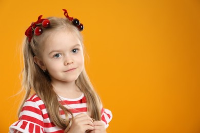 Photo of Cute little girl wearing beautiful bows with cherries on orange background. Space for text