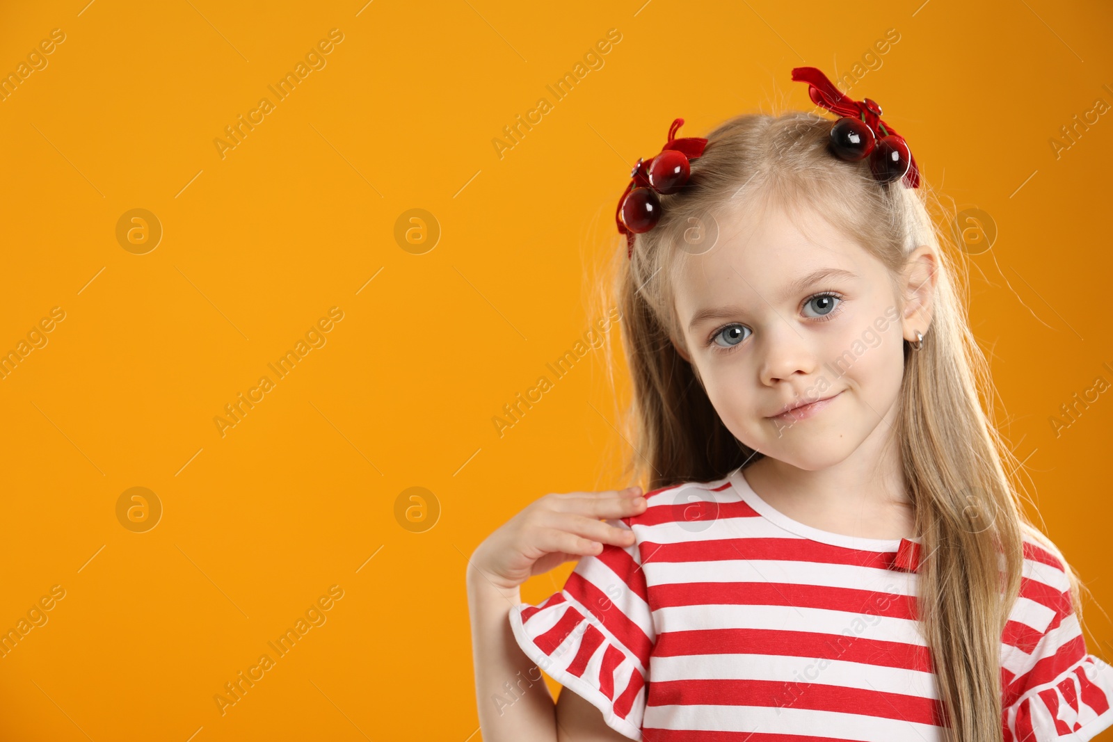 Photo of Cute little girl wearing beautiful bows with cherries on orange background. Space for text