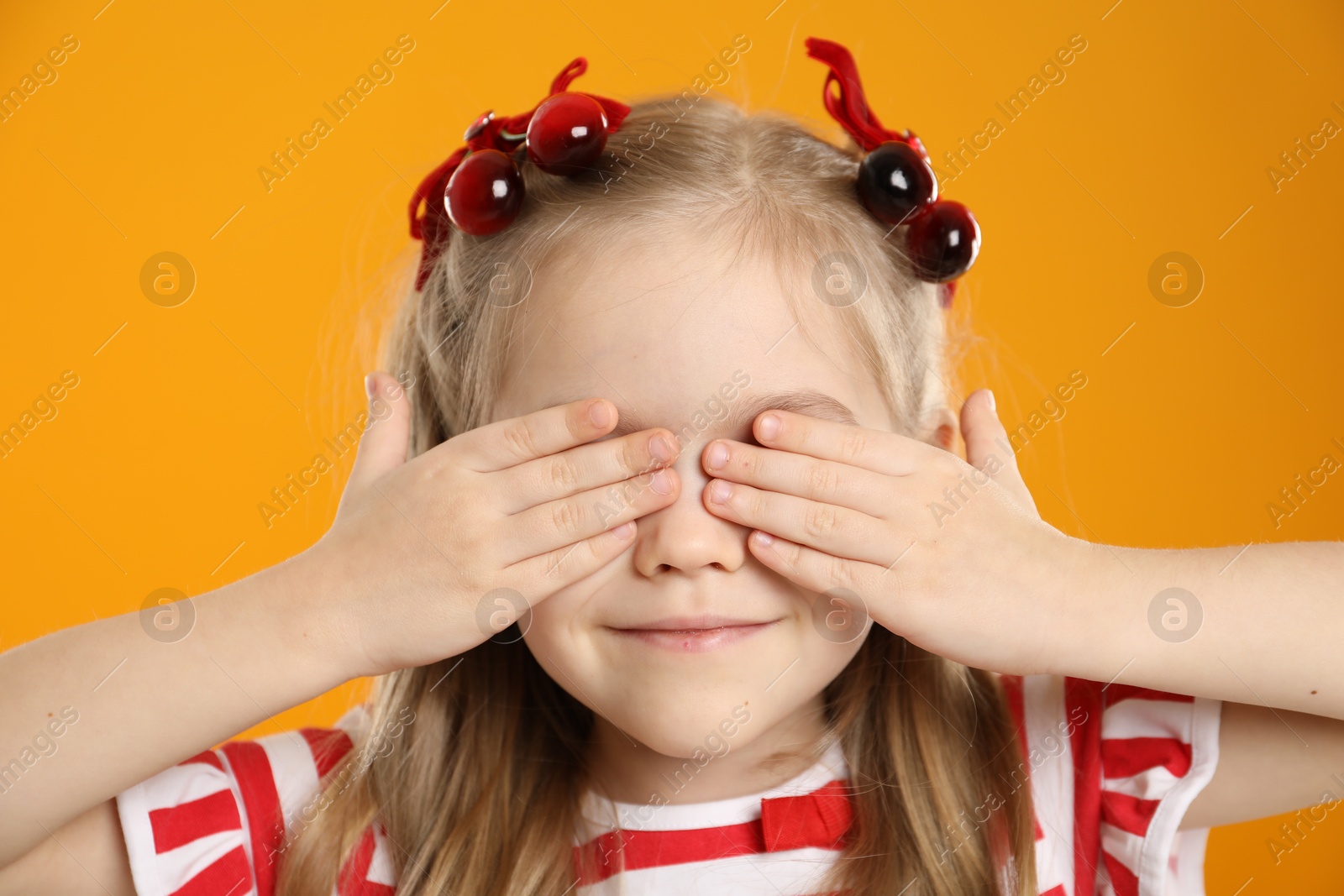 Photo of Cute little girl wearing beautiful bows with cherries on orange background