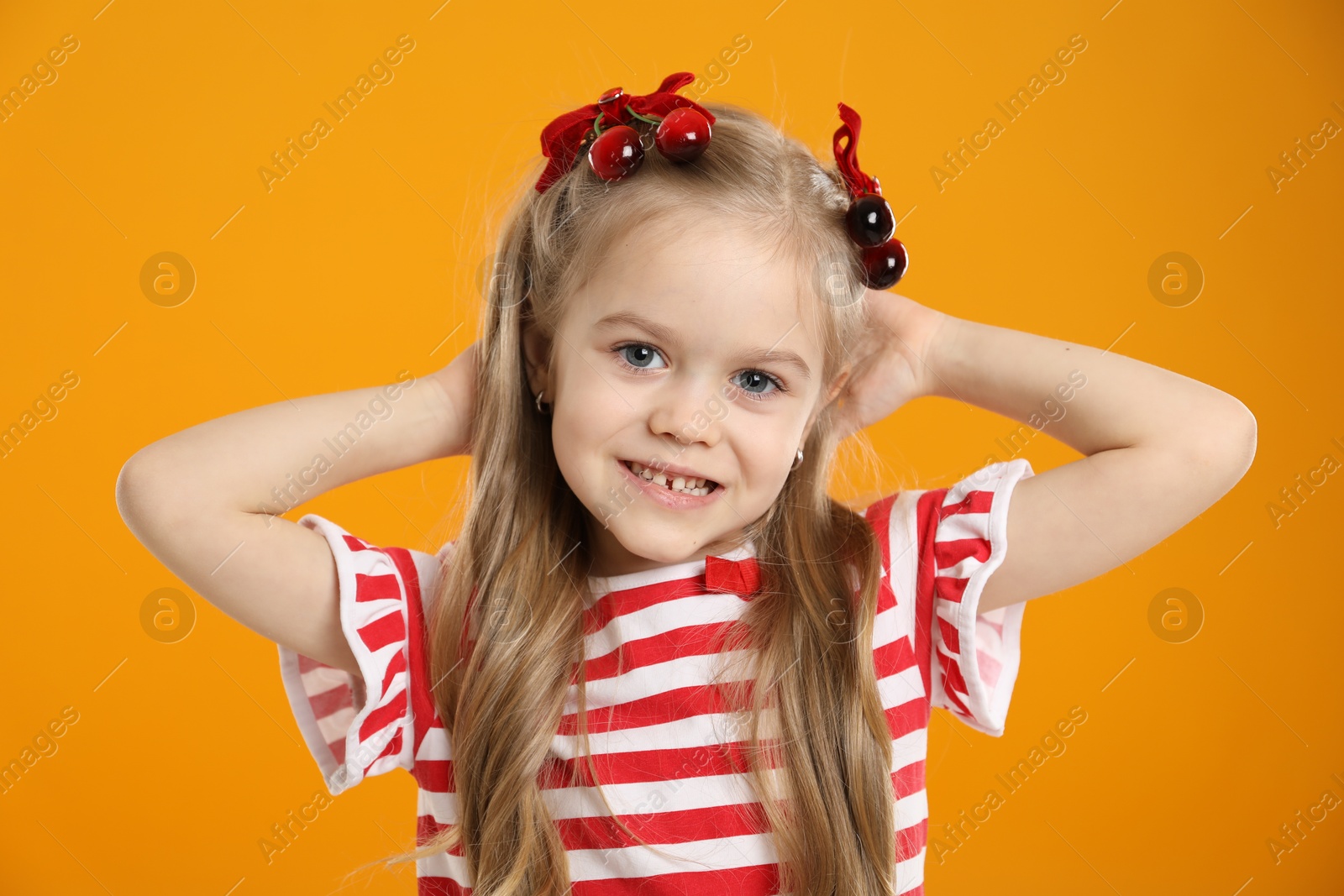 Photo of Cute little girl wearing beautiful bows with cherries on orange background