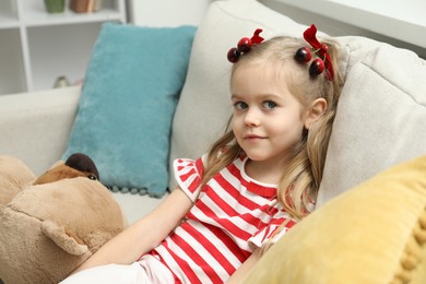 Photo of Cute little girl wearing beautiful bows with cherries on sofa at home