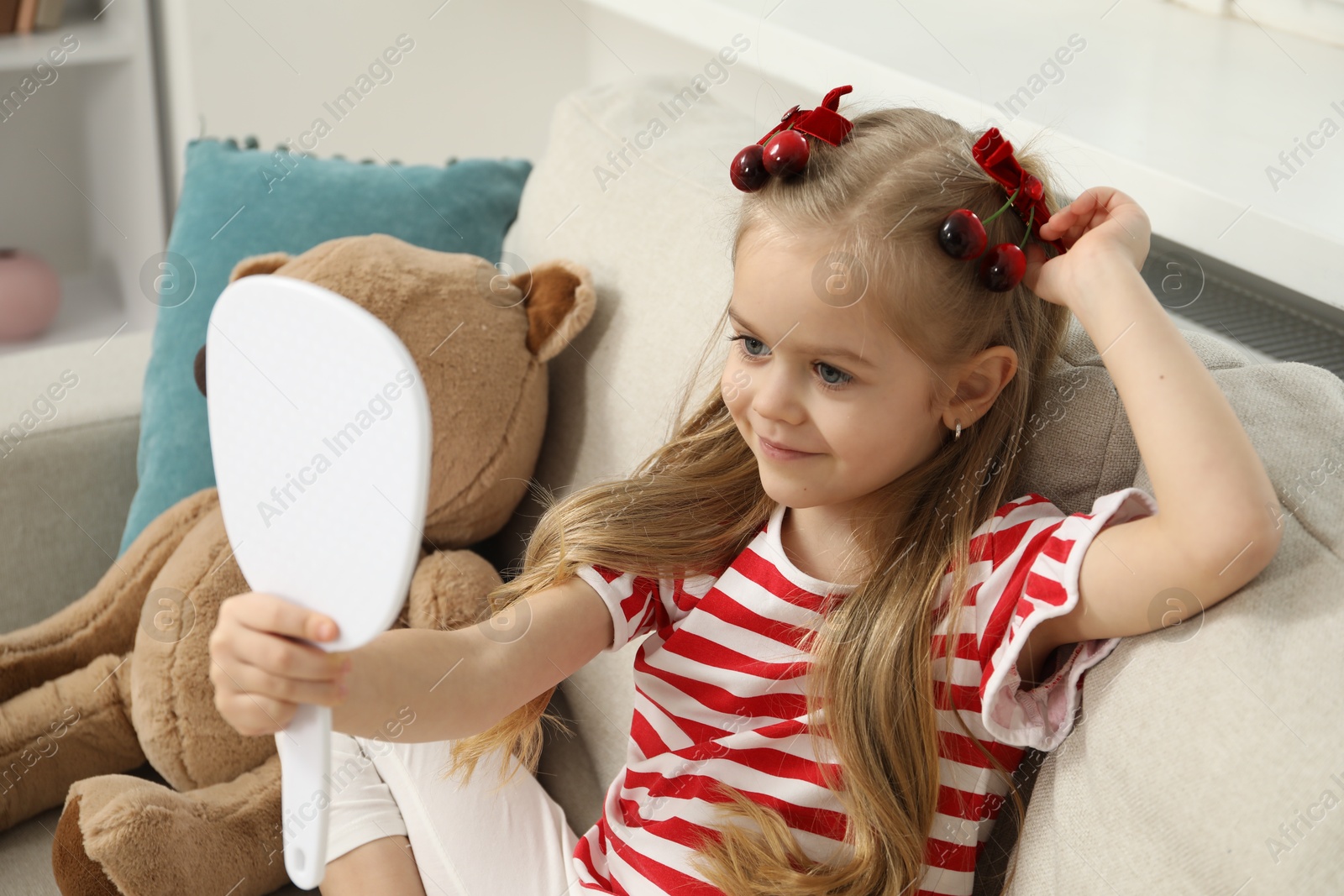 Photo of Cute little girl with beautiful hair clips looking into mirror at home