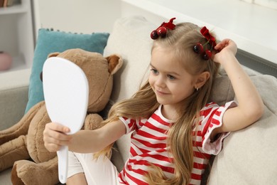 Photo of Cute little girl with beautiful hair clips looking into mirror at home