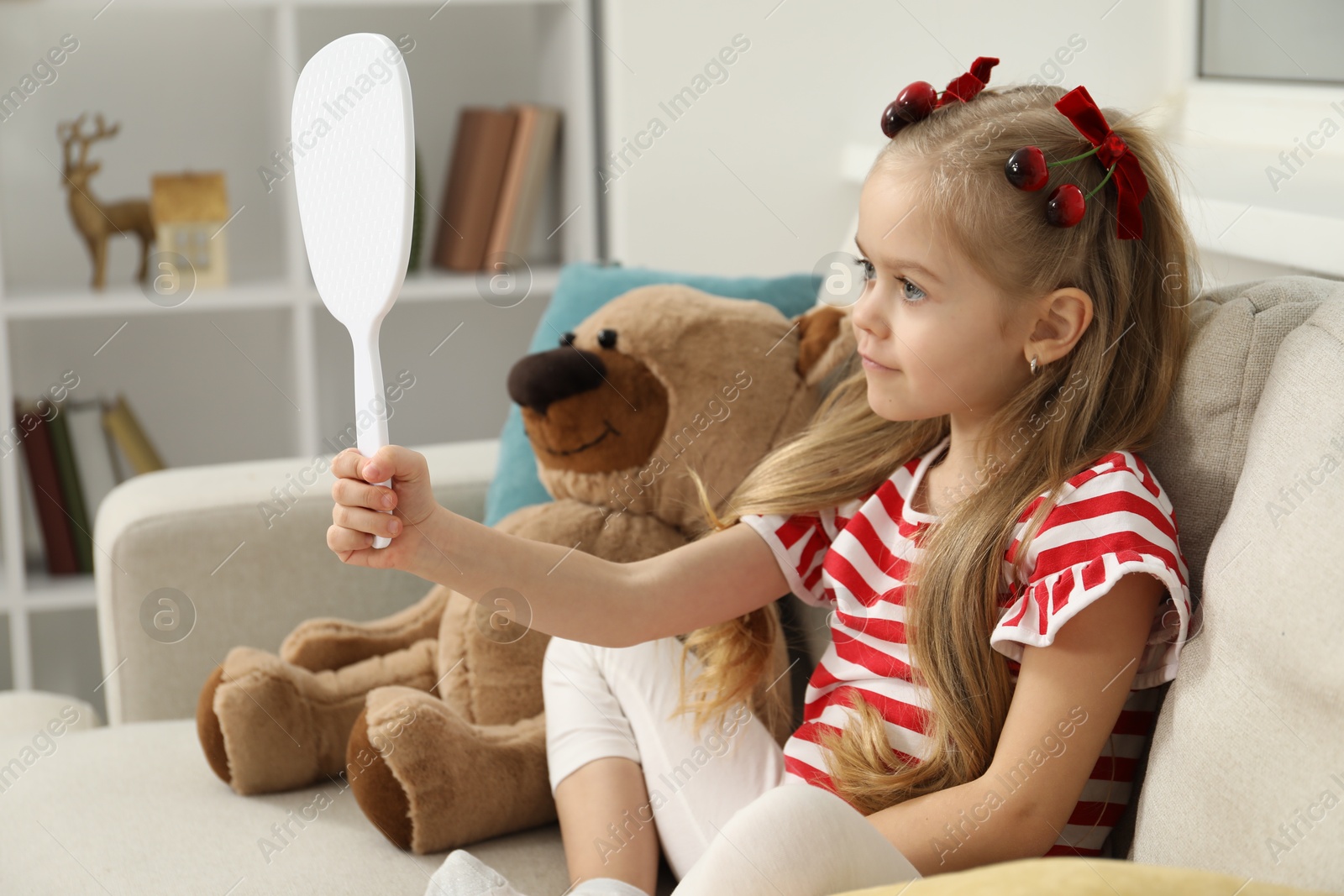 Photo of Cute little girl with beautiful hair clips looking into mirror at home