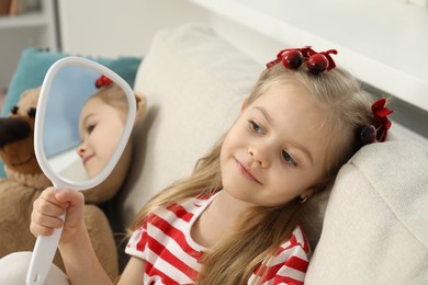 Photo of Cute little girl with beautiful hair clips looking into mirror at home