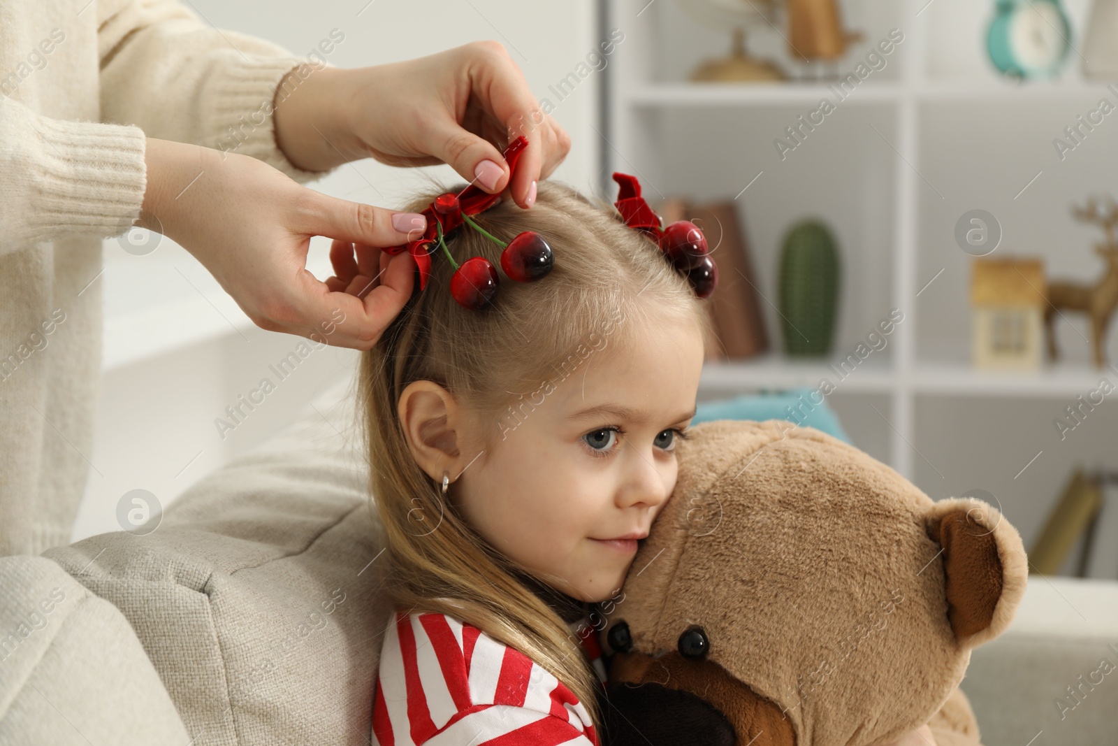 Photo of Mom putting cute accessories onto her daughter's hair at home, closeup