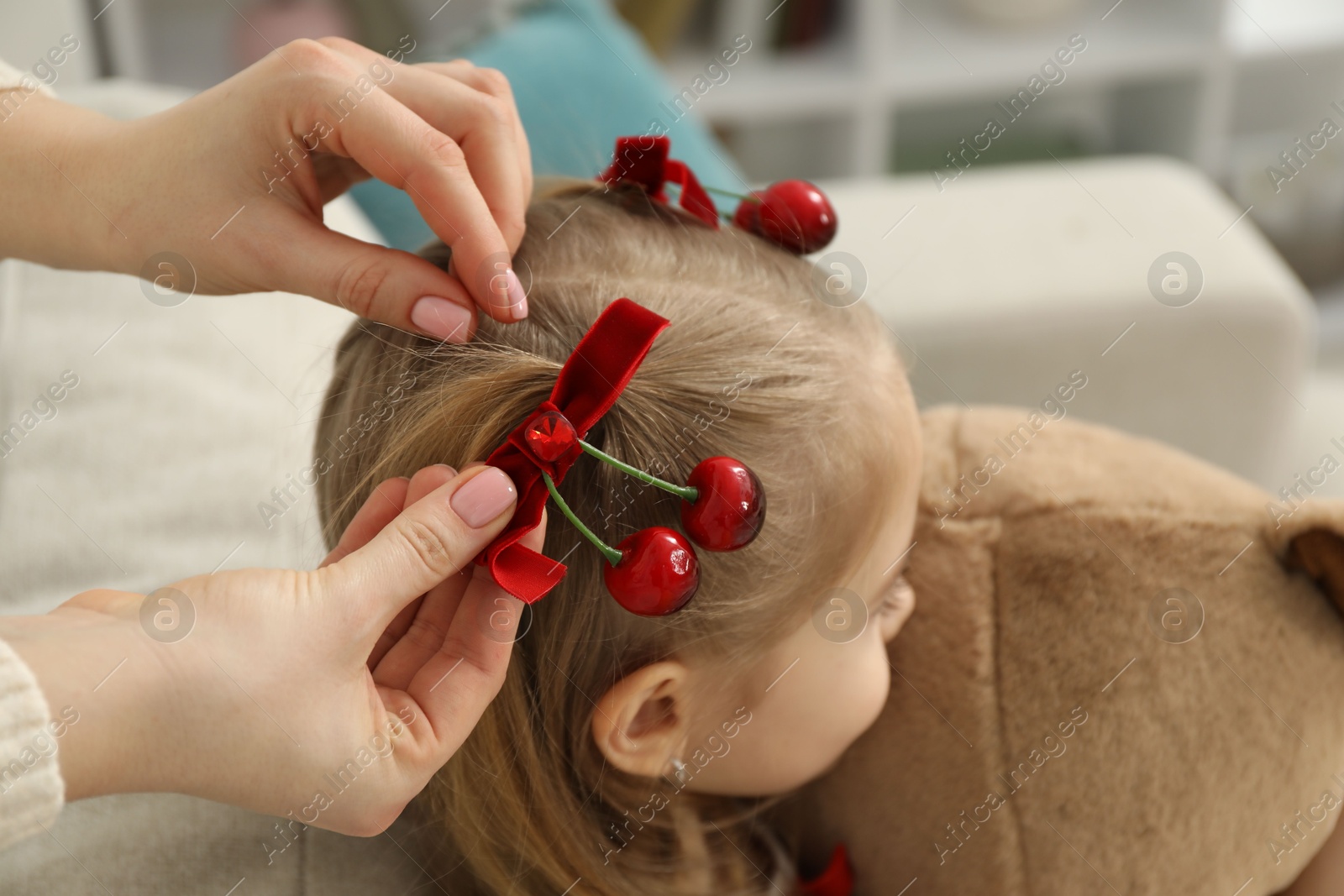 Photo of Mom putting cute accessories onto her daughter's hair at home, closeup