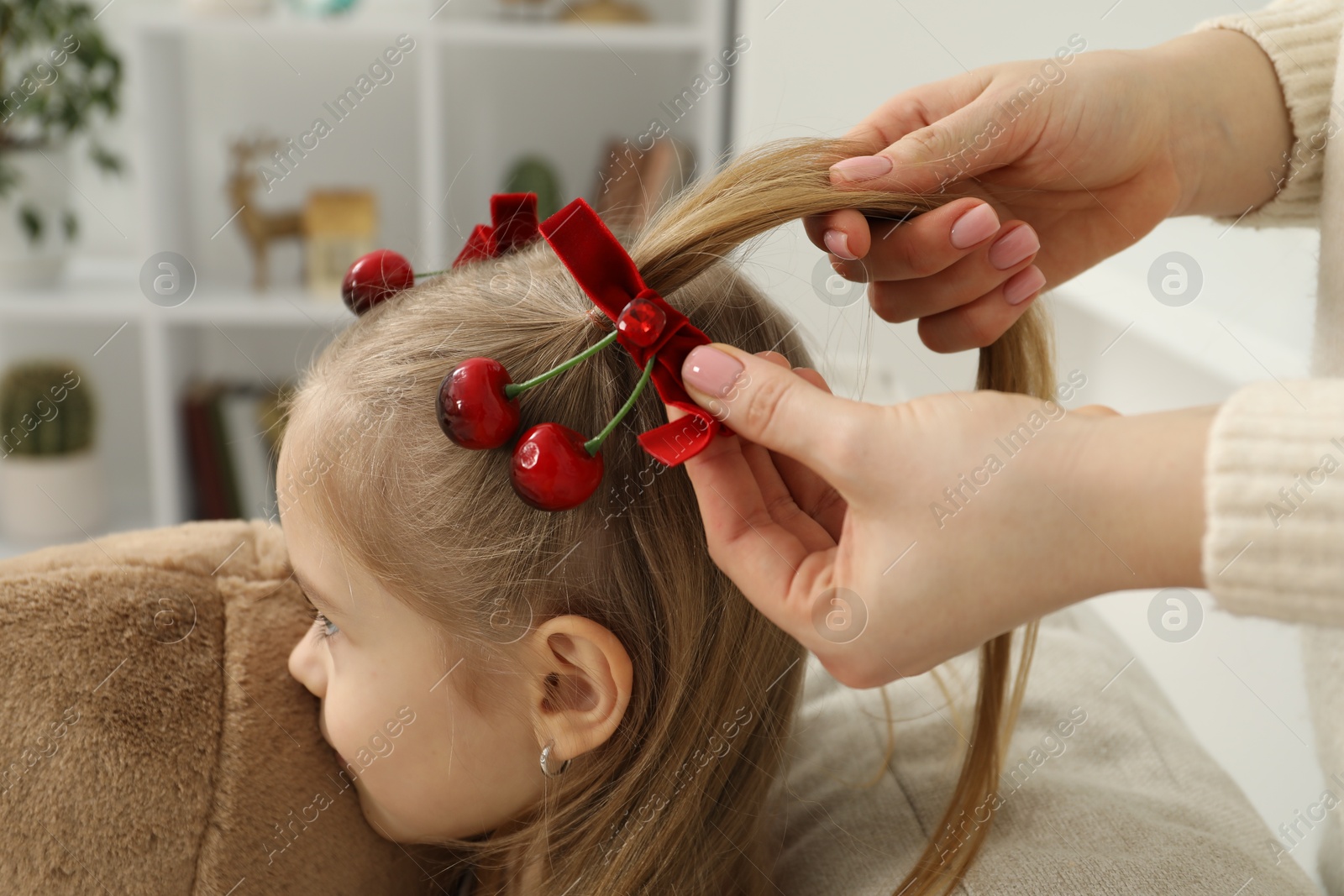 Photo of Mom putting cute accessories onto her daughter's hair at home, closeup