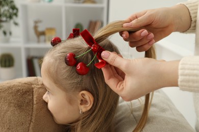 Photo of Mom putting cute accessories onto her daughter's hair at home, closeup