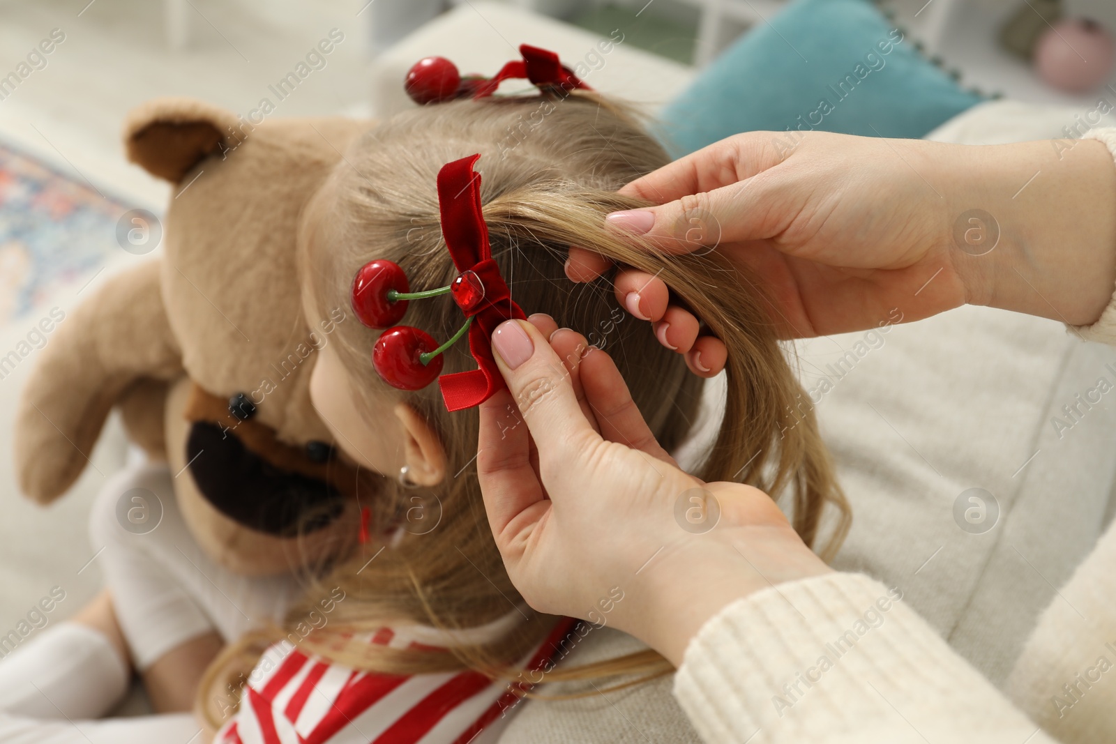 Photo of Mom putting cute accessories onto her daughter's hair at home, closeup