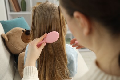 Photo of Mother brushing her little daughter's hair at home, closeup