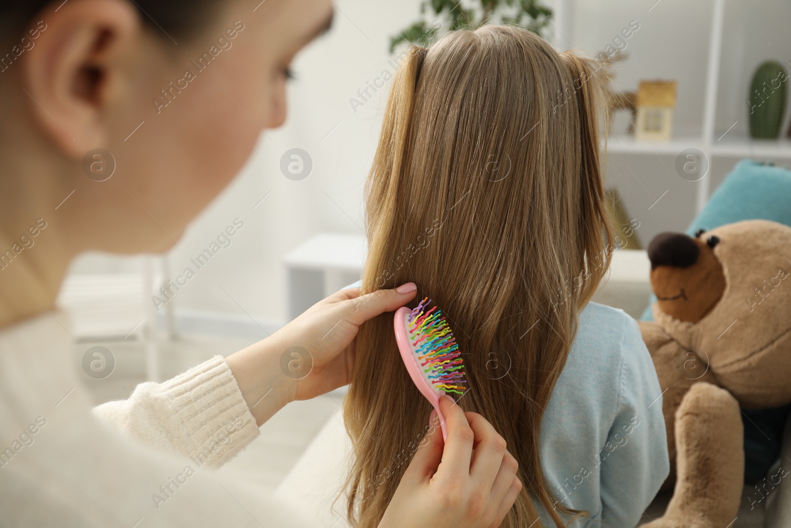 Photo of Mother brushing her little daughter's hair at home, closeup