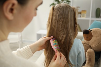 Photo of Mother brushing her little daughter's hair at home, closeup