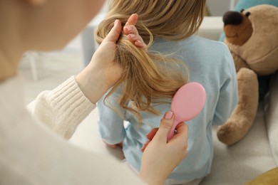 Photo of Mother brushing her little daughter's hair at home, closeup