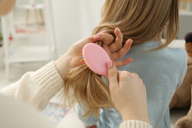 Photo of Mother brushing her little daughter's hair at home, closeup