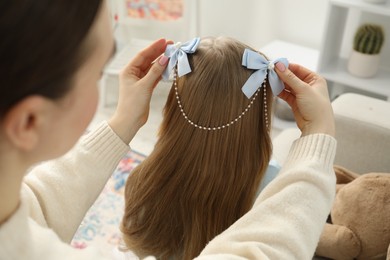 Photo of Mom putting cute accessories onto her daughter's hair at home, closeup