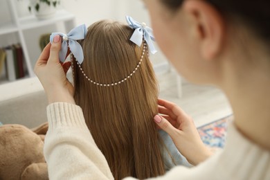 Photo of Mom putting cute accessories onto her daughter's hair at home, closeup