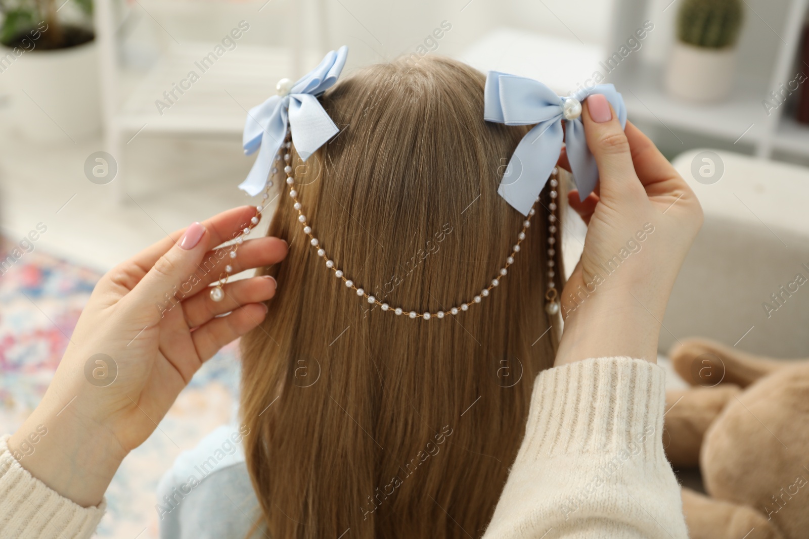 Photo of Mom putting cute accessories onto her daughter's hair at home, closeup