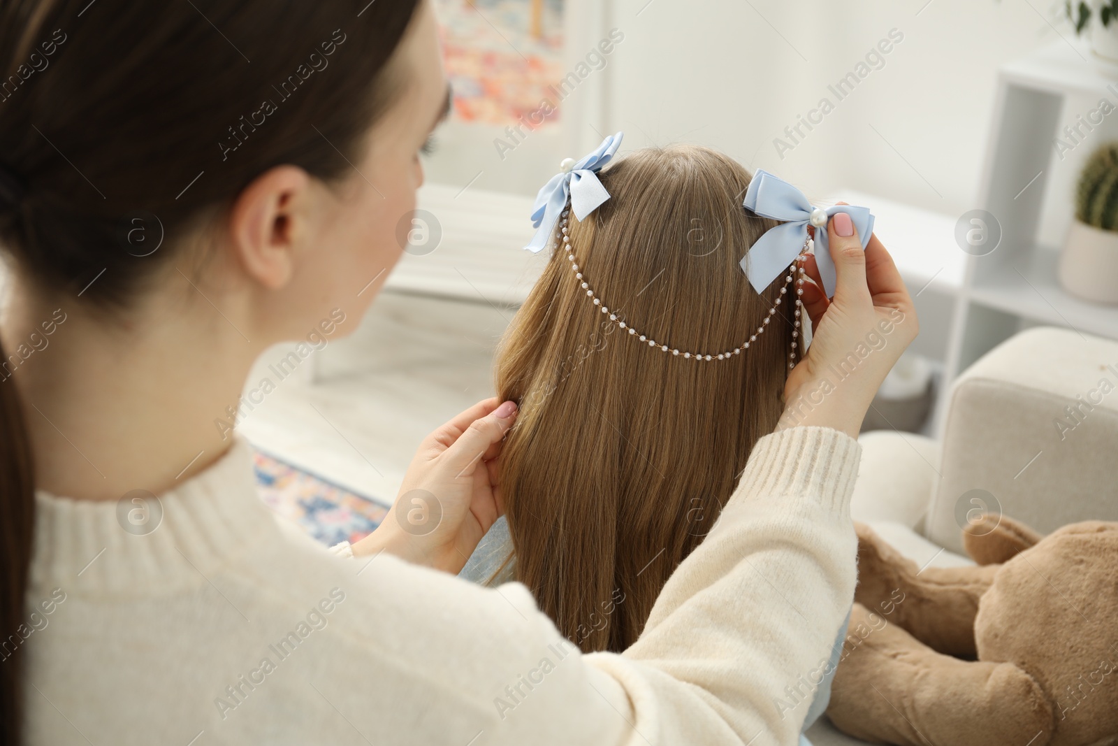 Photo of Mom putting cute accessories onto her daughter's hair at home, closeup