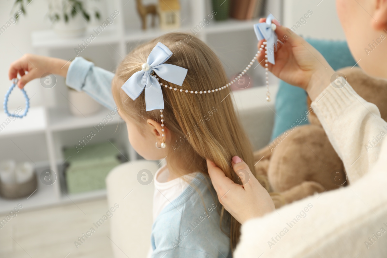 Photo of Mom putting cute accessories onto her daughter's hair at home, closeup