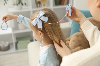 Photo of Mom putting cute accessories onto her daughter's hair at home, closeup