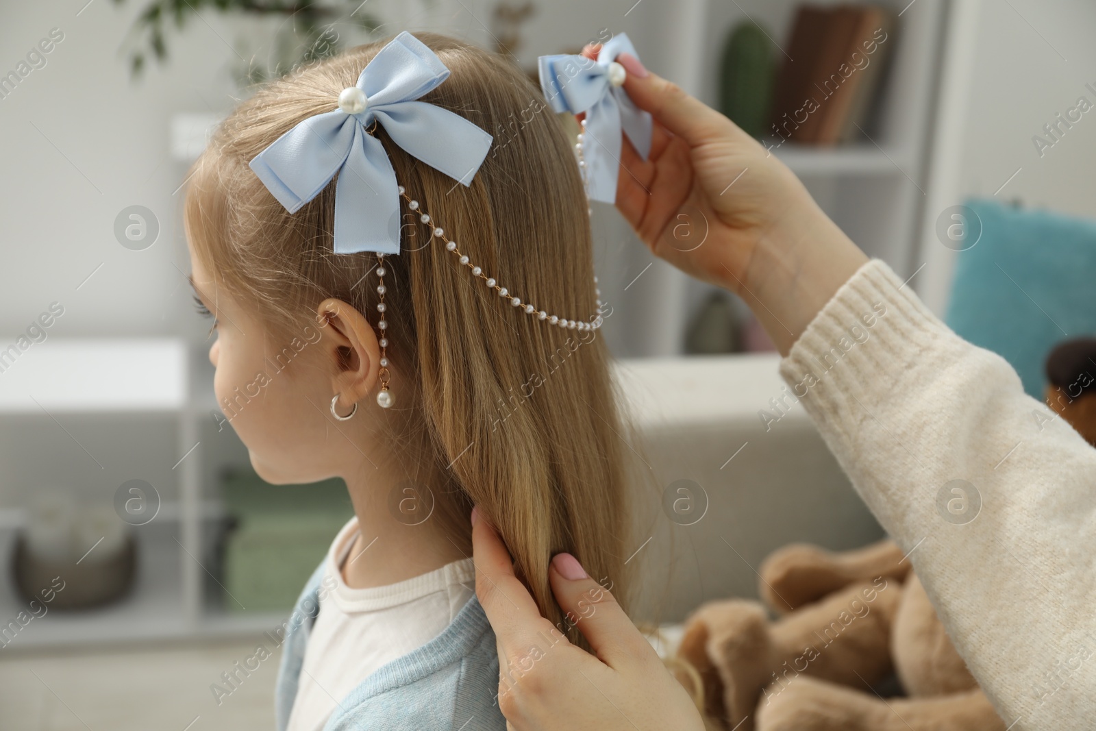 Photo of Mom putting cute accessories onto her daughter's hair at home, closeup