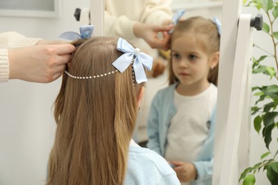 Photo of Mom putting cute accessories onto her daughter's hair at home, closeup