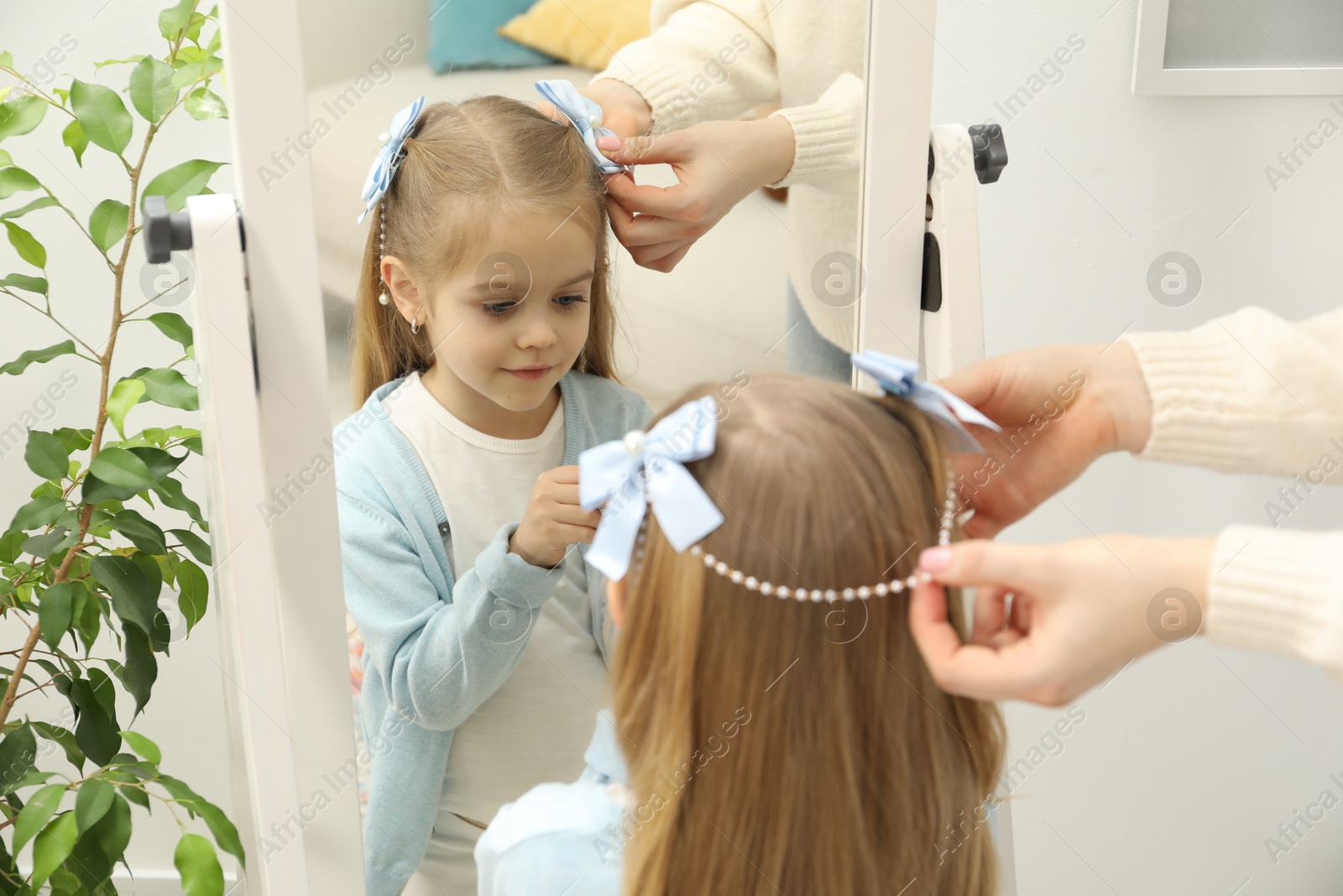 Photo of Mom putting cute accessories onto her daughter's hair at home, closeup