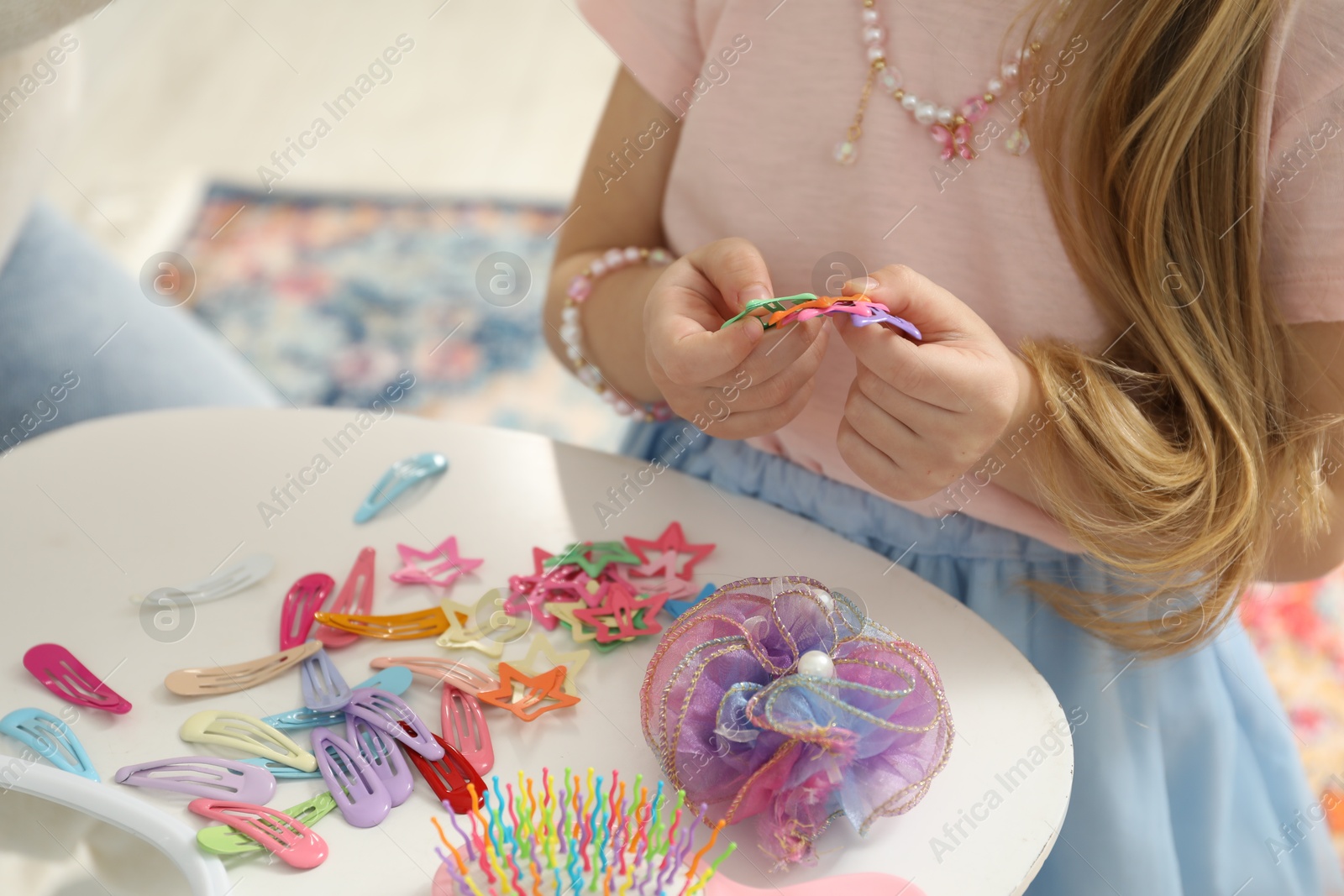 Photo of Little girl with many cute hair accessories at table indoors, closeup