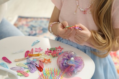 Photo of Little girl with many cute hair accessories at table indoors, closeup