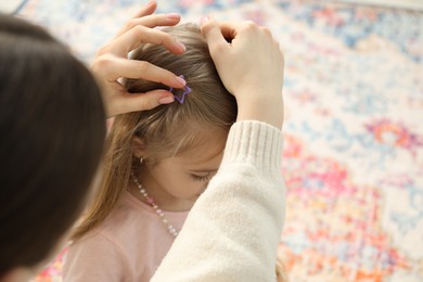 Photo of Mom putting cute accessories onto her daughter's hair at home, closeup