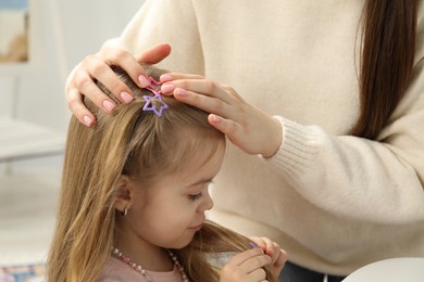 Photo of Mom putting cute accessories onto her daughter's hair at home, closeup