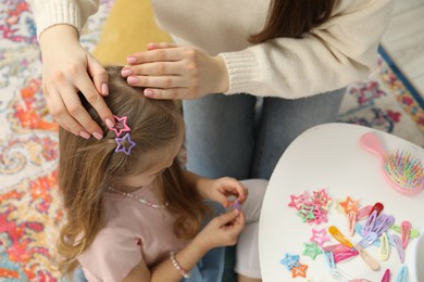 Photo of Mom putting cute accessories onto her daughter's hair at home, closeup